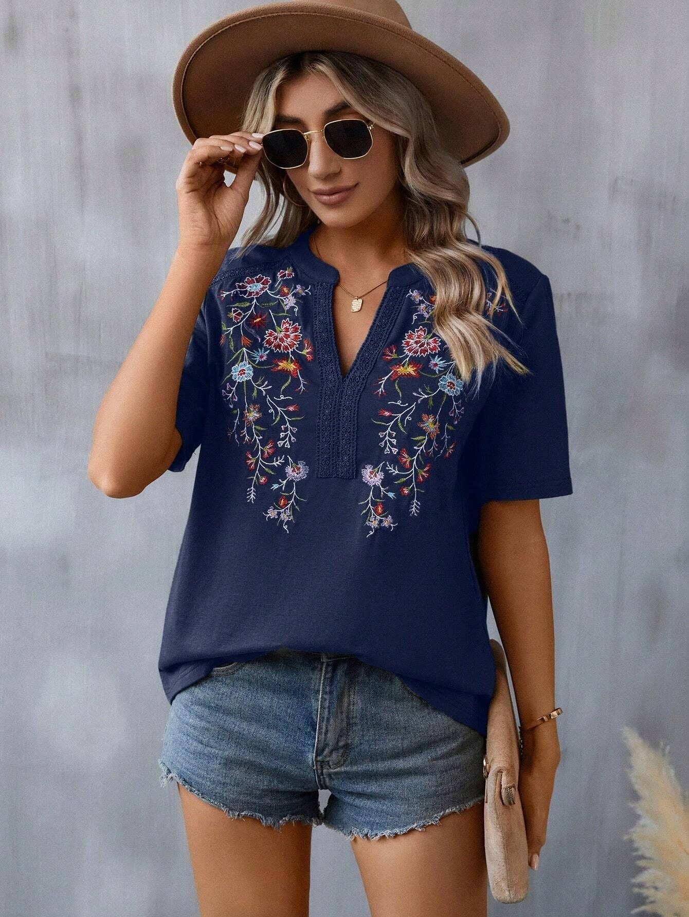 Woman in navy blue embroidered floral top, denim shorts, and hat. Summer boho fashion.